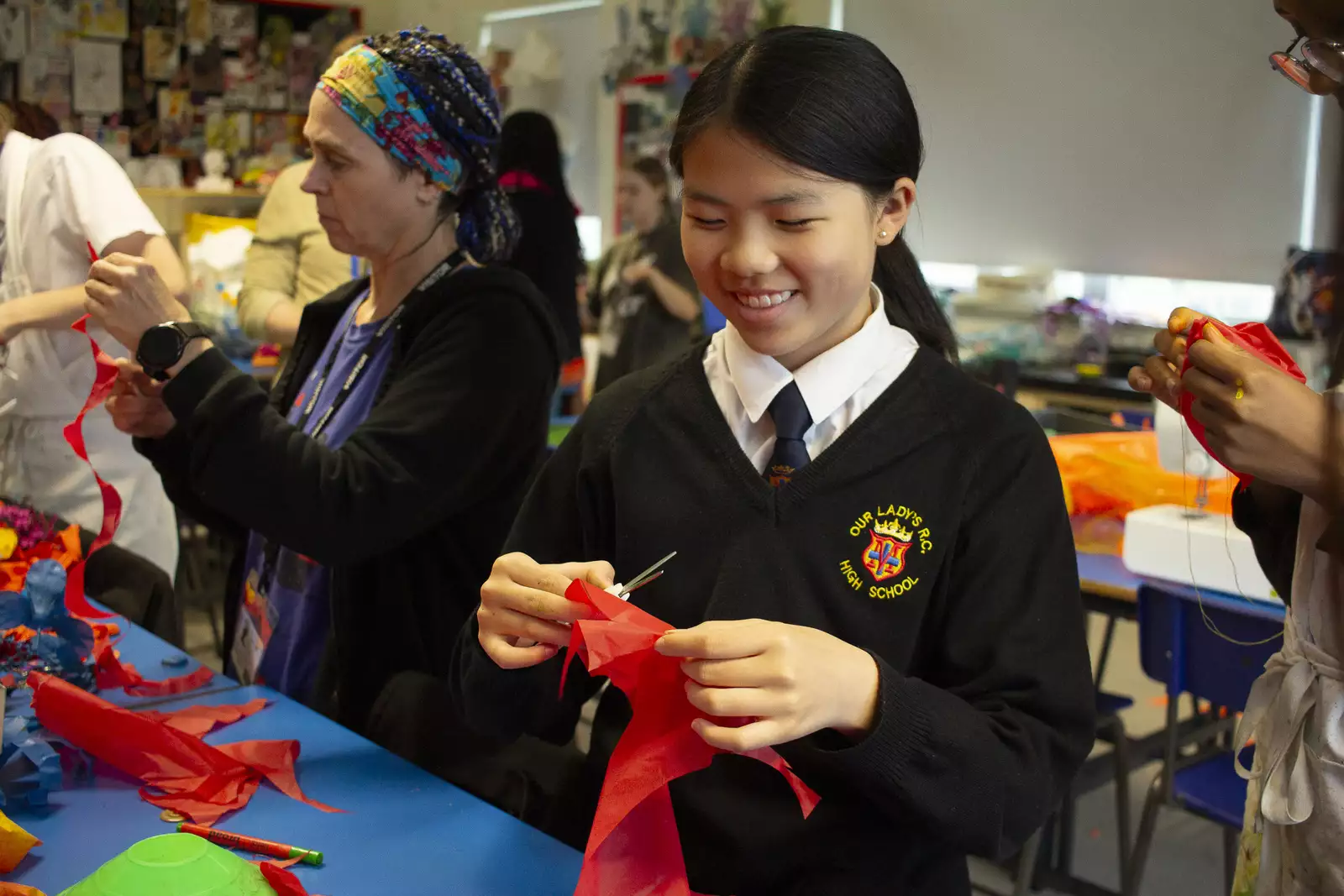 A child smiles during a craft session, holding scissors and red paper