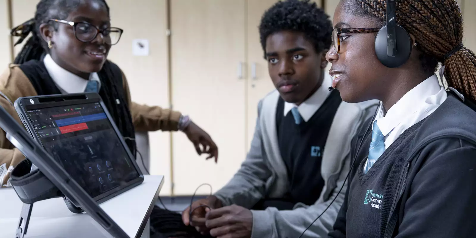 Three children sat around an iPad, one wearing headphones