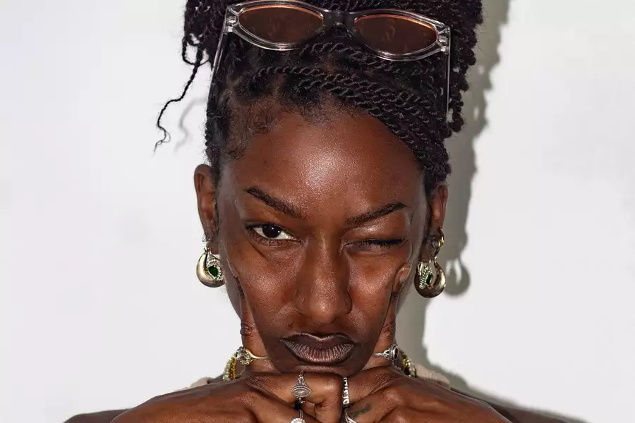 Meme Gold looks at the camera wearing rings and a light tank top