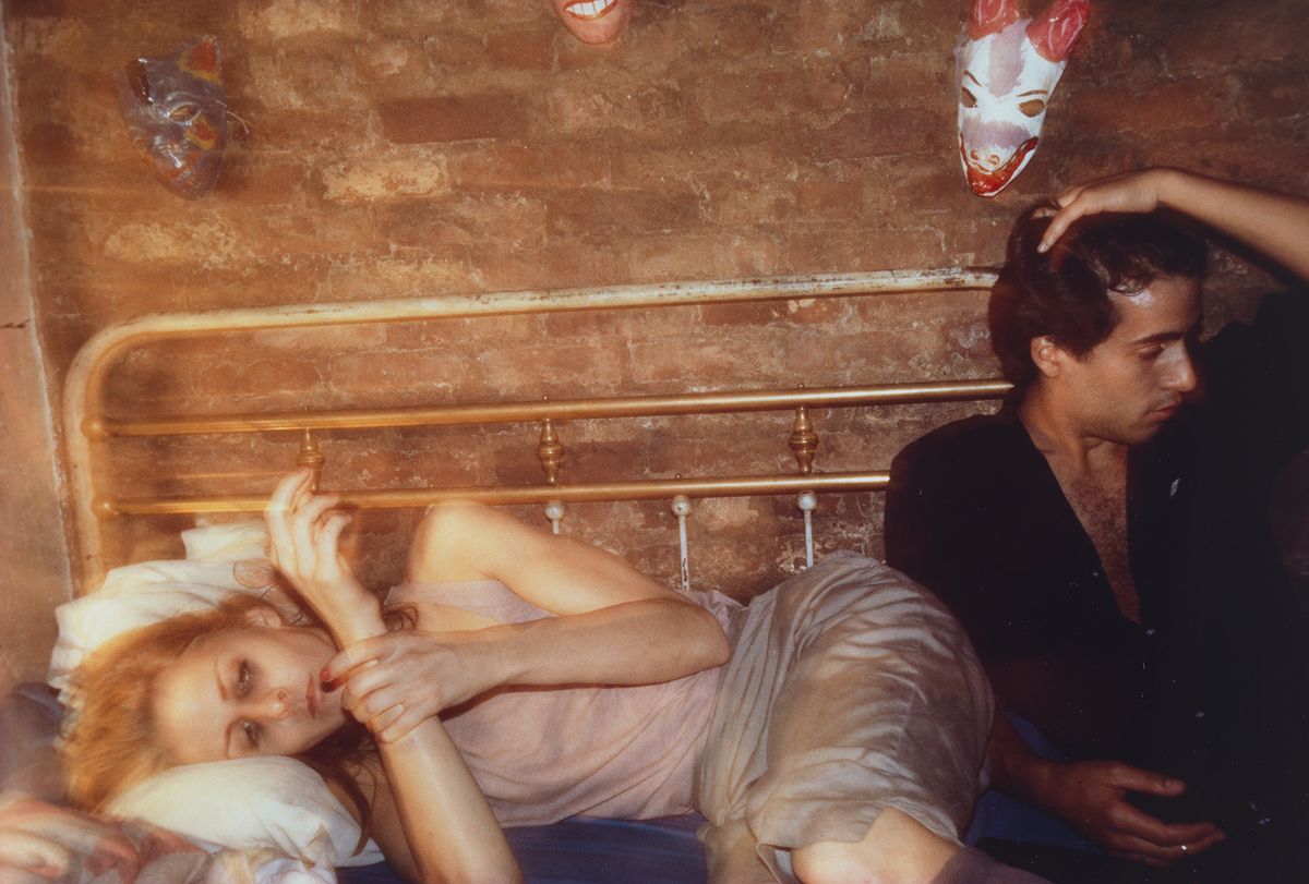 Cibachrome colour photograph of a woman lying on a bed. A man sits next to her, facing away.