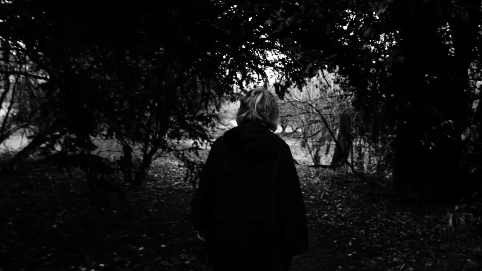 black and white photo of a woman walking through a forest