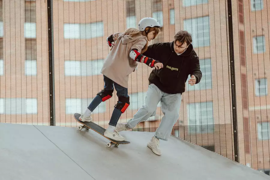 Photo of an instructor teaching a young person to skateboard on a ramp