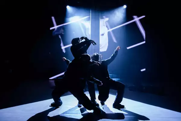 Three dancers dancing on stage around a pole during Traplord, with a projection behind them.