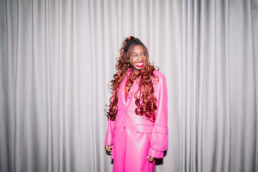 Factory+ Editor in Residence Kemi Alemoru wears a pink trench coat and smiles at the camera