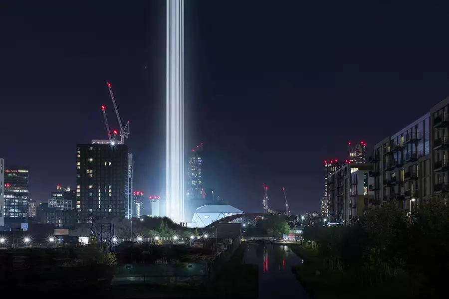 A Manchester cityscape at nighttime with bright columns of light visible next to the Factory International building.