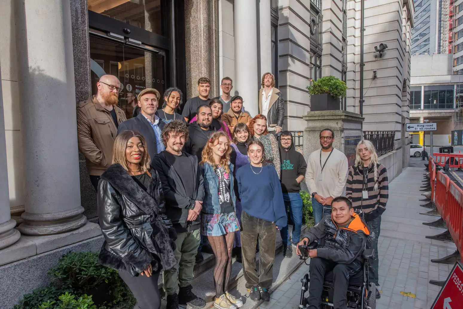 A group of people stand in front of an entrance to an office building, smiling and looking towards the camera.