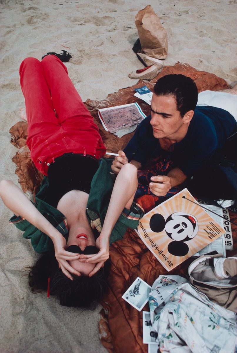 Friends of artist Nan Goldin laying on the beach on a picnic rug.