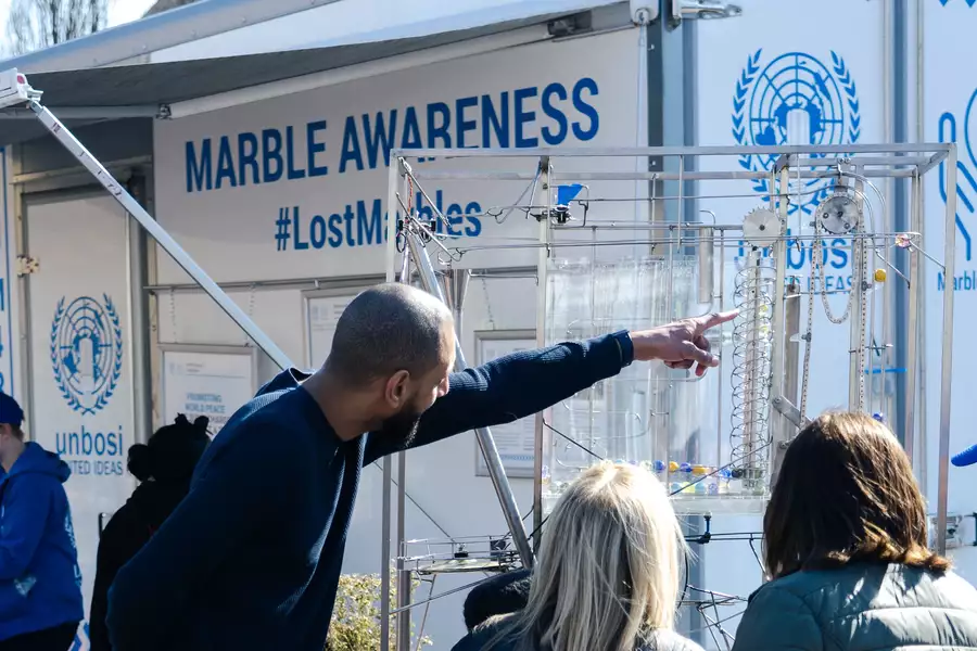 A person pointing at a marble run in front of a trailer with the words 'Marble Awareness. #LostMarbles' on