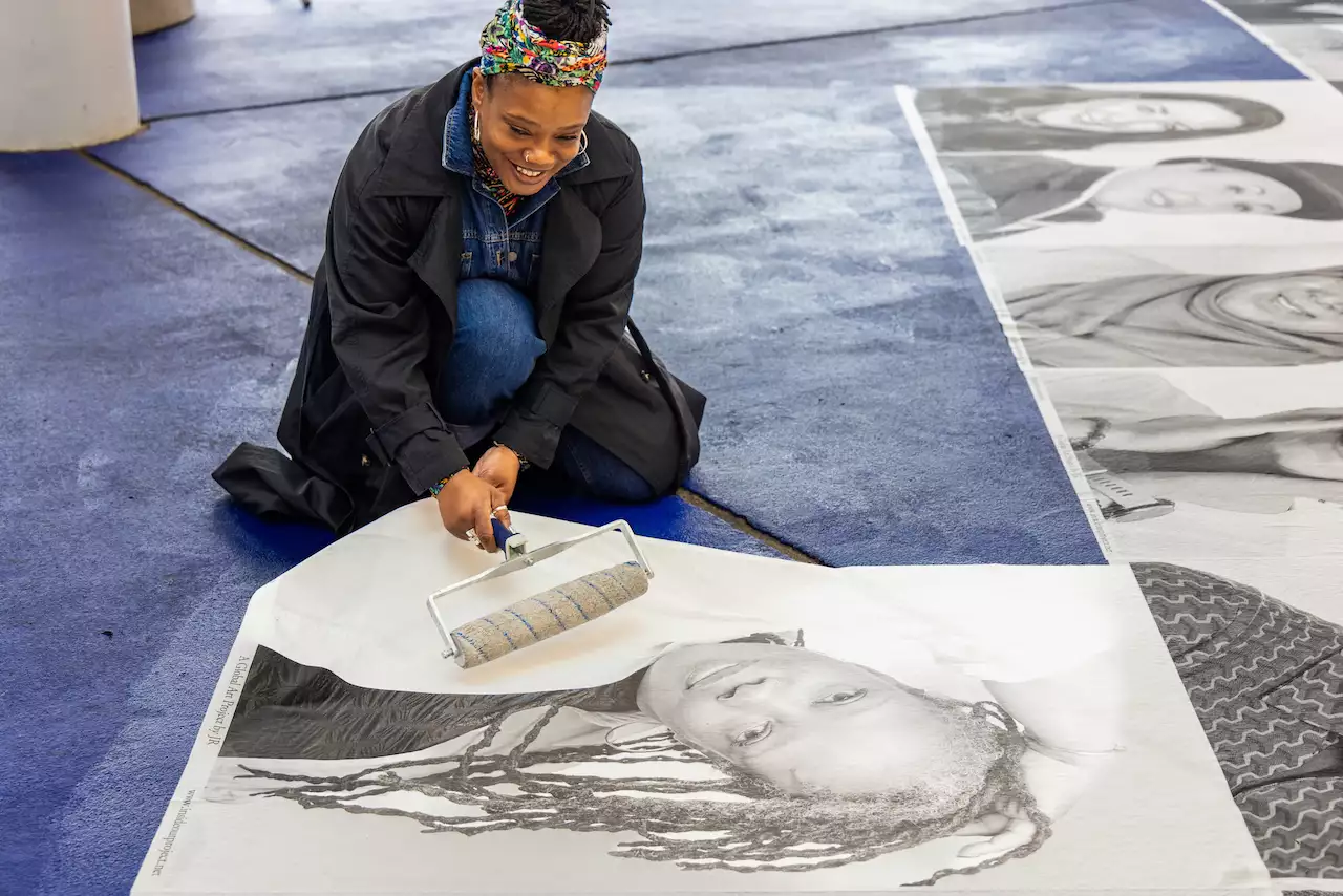 Someone installing a portrait from Inside Out on the ground and smiling