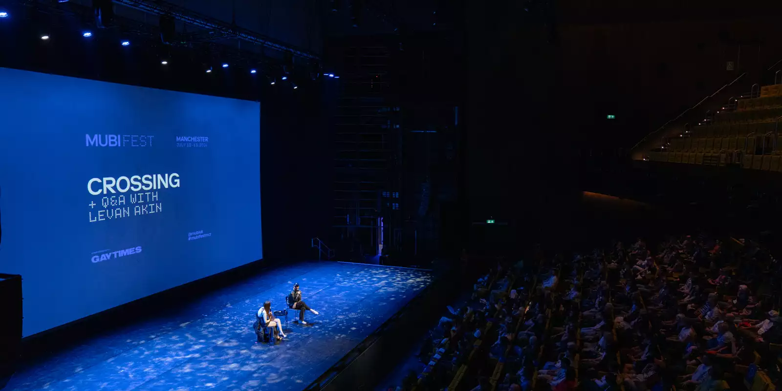 Film showing of 'Crossing' in the Hall. Two people are sat on stage for the Q&A in front of the big screen. The lighting is blue.