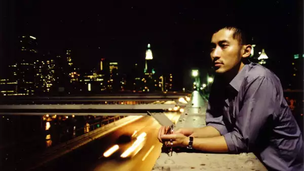 Huang Ruo stood on a bridge above a motorway, with the bright lights of a city behind him
