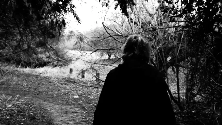 black and white photo of a woman walking through a forest