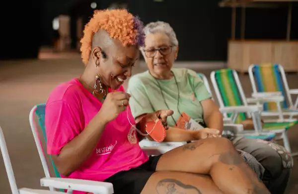 Two people sat on deck chairs sewing and smiling