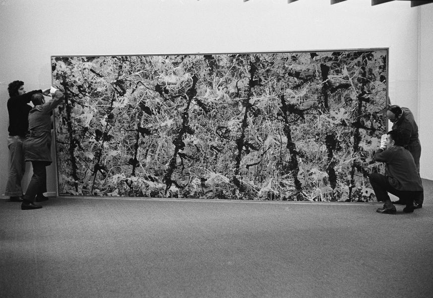 A black and white image of art handlers installing iconic painting blue poles