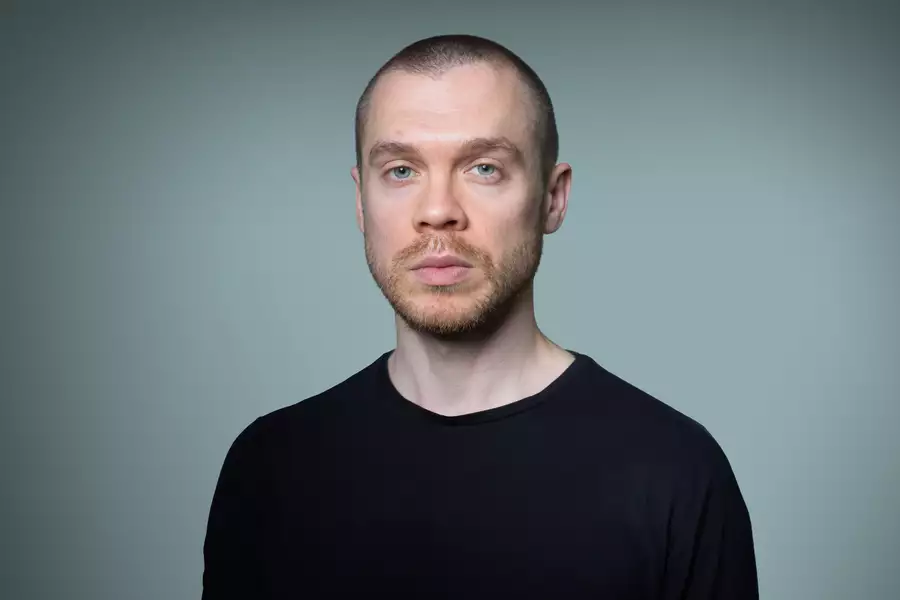 A headshot of Gary Stevenson with short hair and a neatly trimmed beard, wearing a plain black T-shirt. The background is a smooth gradient of gray-green.