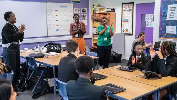 A group of students and teachers clapping in a classroom