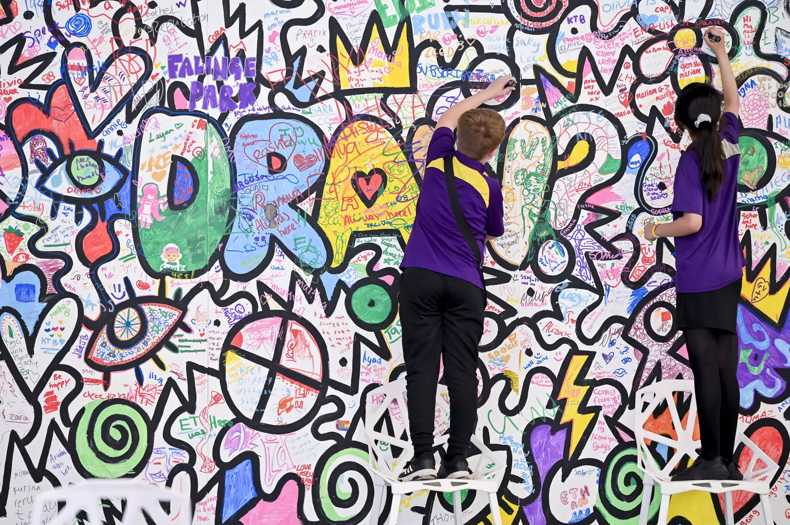 Two children drawing on a colourful doodle wall