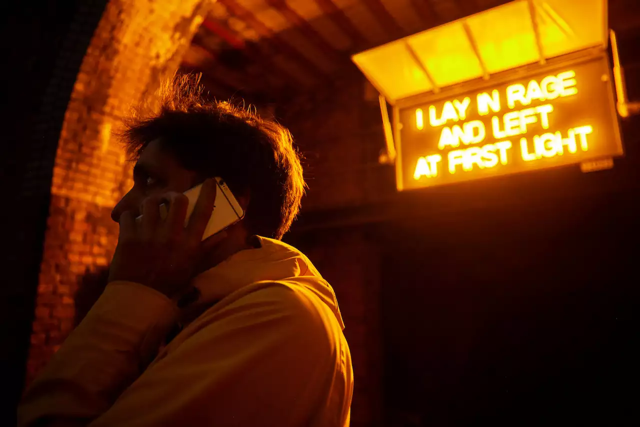 A person on the phone with the words 'I lay in rage and left at first light' illuminated behind them