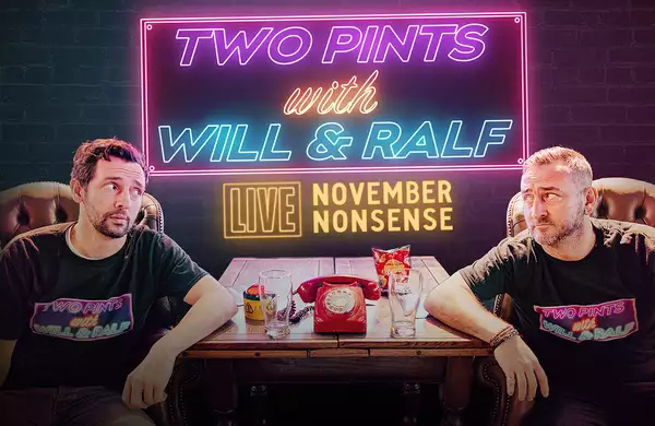 A promotional poster for Two Pints with Will & Ralf – LIVE: November Nonsense. Will Mellor and Ralf Little sit in a pub-like setting, wearing matching black T-shirts with the show's logo. A wooden table between them holds pints, a red phone, and snacks. The background features a dark brick wall with neon-style signage in pink, blue, and yellow displaying the show's title.