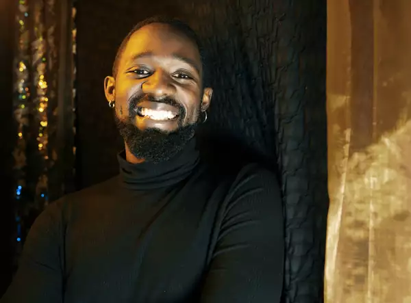 A headshot of artist and dancer Ziza Patrick wearing a black rollneck and smiling at the camera