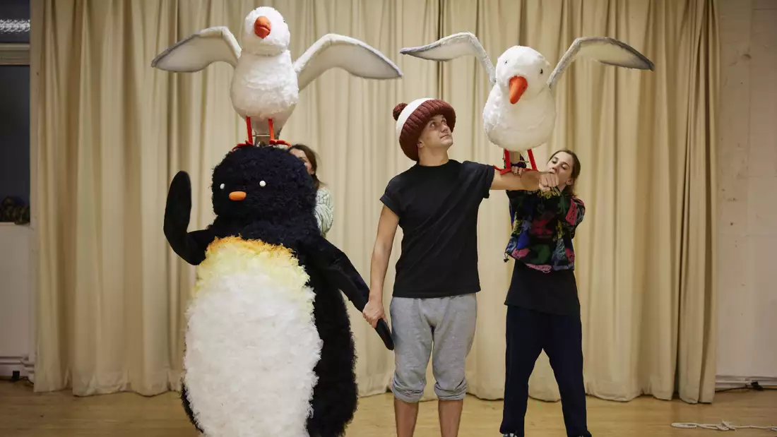 Adult size penguin costume and actor in giant bobble hat with a puppet penguin on his arm