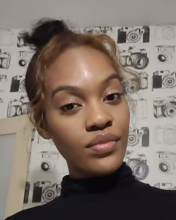 Shemel Rose-Thompson wearing a black turtleneck top. The background shows wallpaper with pictures of cameras.