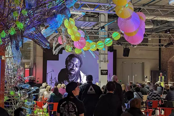 People gathered in the Social at Aviva Studios watching a film on the big screen. There is a colourful sculpture on display.