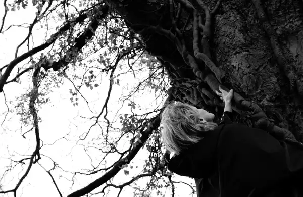 black and white photo of a woman looking up at a large tree trunk
