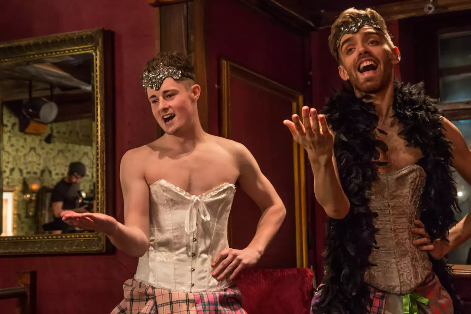 Two performers in corsets sing in an ornate room