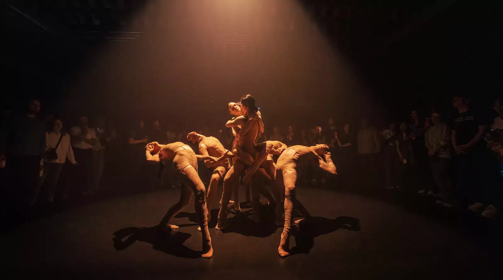 Photo of six dancers entwined with a circle of people around them watching
