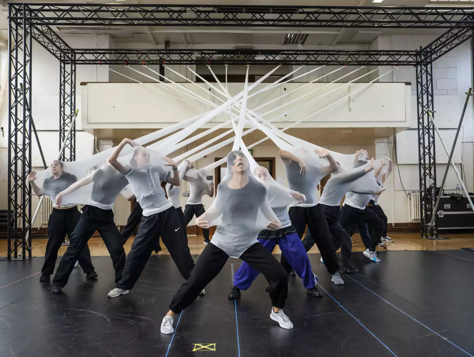 Dancers in stretched white fabric attached to a rig in rehearsals for Free Your Mind