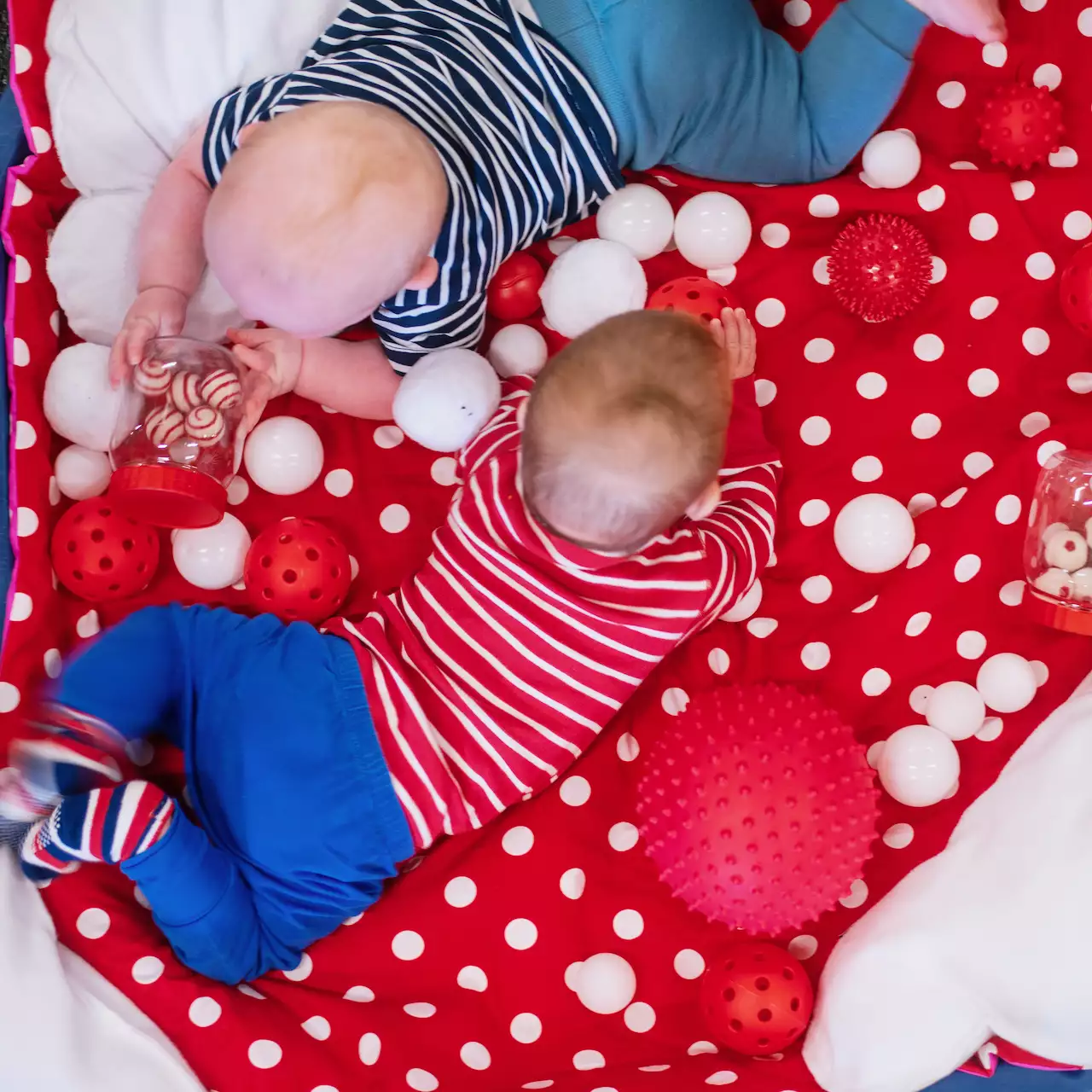 Two babies lying on a red and white dotted mat