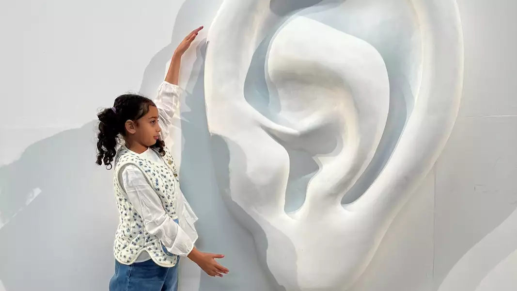 A girl stood next to the giant ear with her hands around it