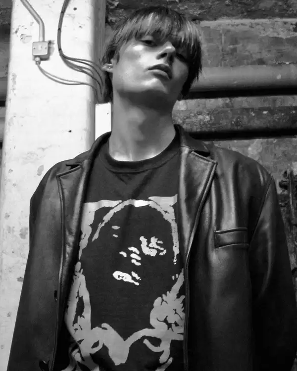 Black and white photo of Gabriel Evans wearing a black leather jacket and looking down at the camera