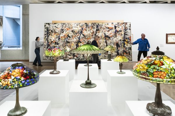 Blue poles carried by conservators behind a display of Tiffany lamps