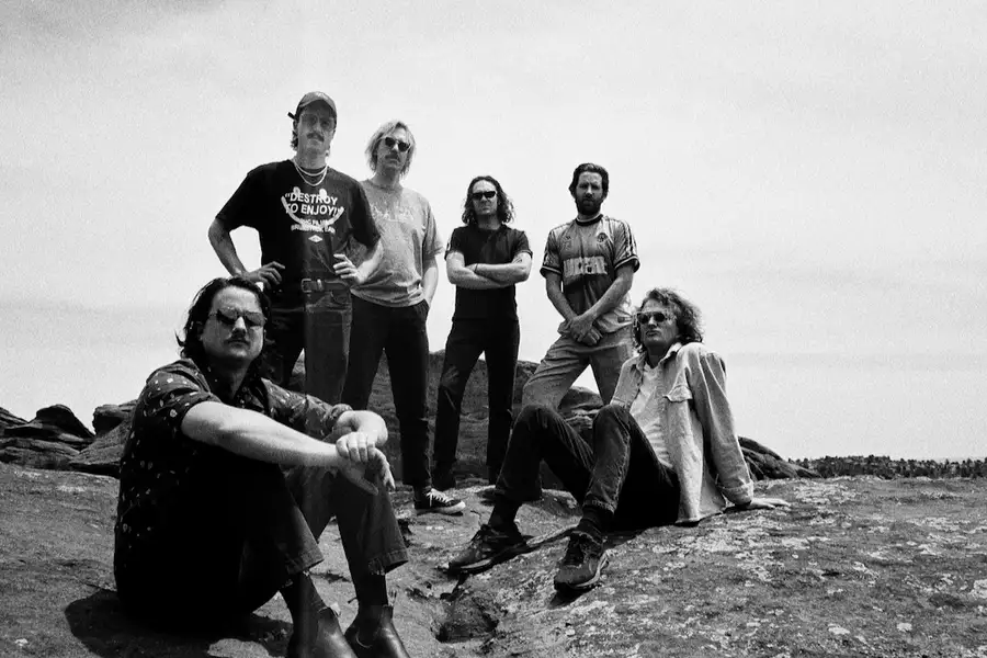 A black and white photo of six members of King Gizzard & The Lizard Wizard posing on a rocky landscape.