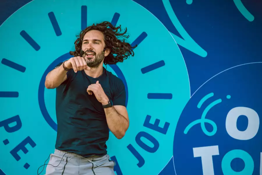 Joe Wicks leading a workout in front of a sign that says 'P.E. with Joe'