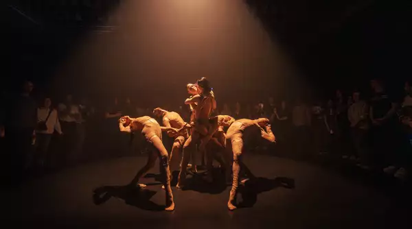 Photo of six dancers entwined with a circle of people around them watching