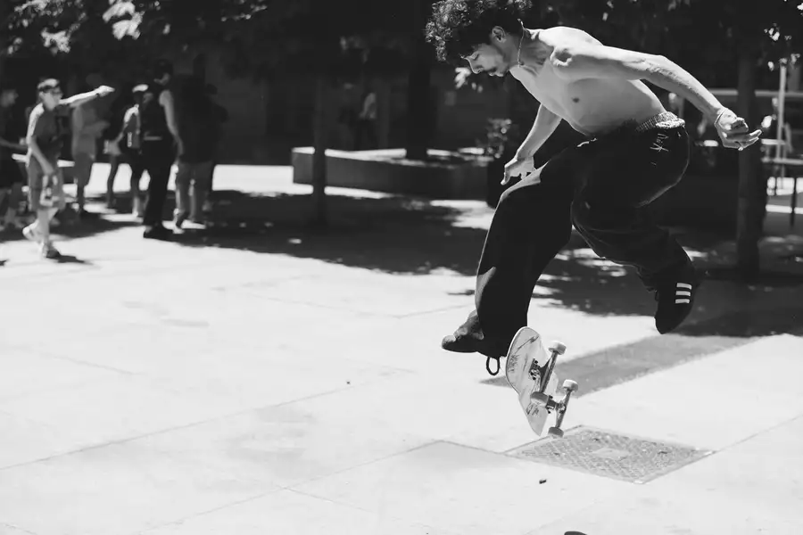 Black and white photograph of a skateboarder mid-trick wearing black adidas trainers