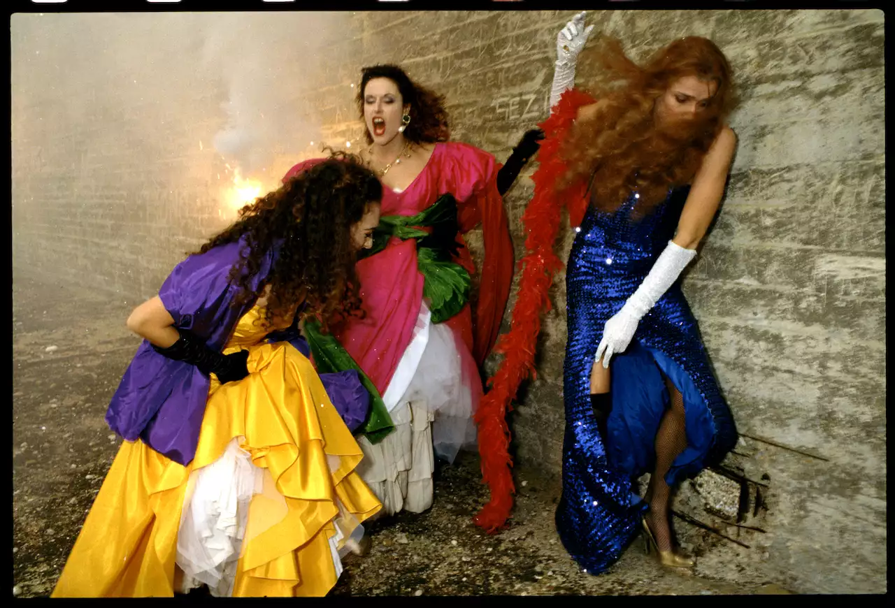Still from Derek Jarman's The Garden (1990), showing three women dressed in brightly coloured ballgowns. There is a fire behind them and they are screaming.
