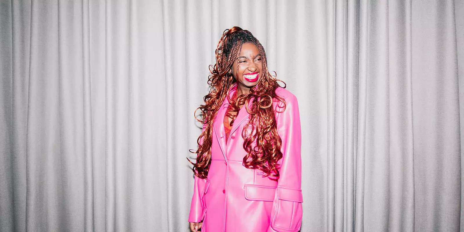 Factory+ Editor in Residence Kemi Alemoru wears a pink trench coat and smiles at the camera
