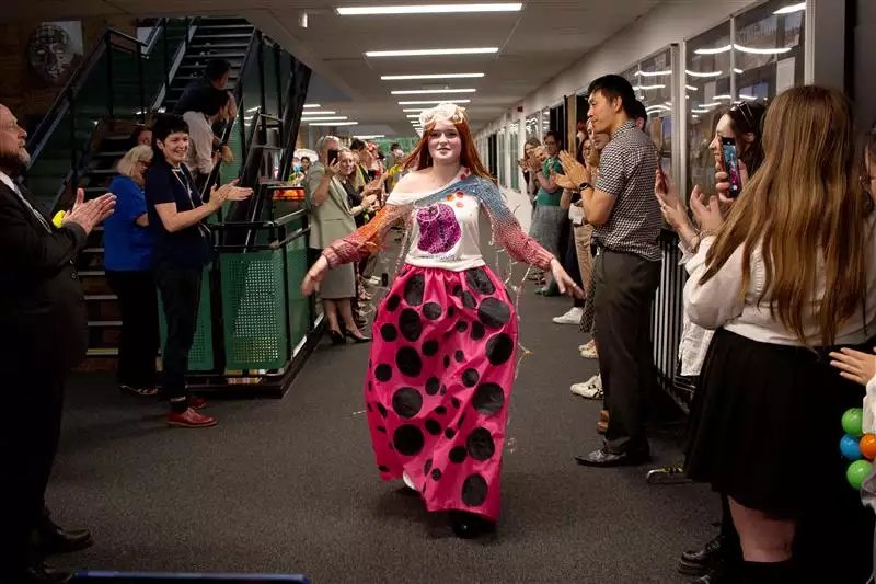 A child walks down a corridor in a school fashion show, with people watching and clapping