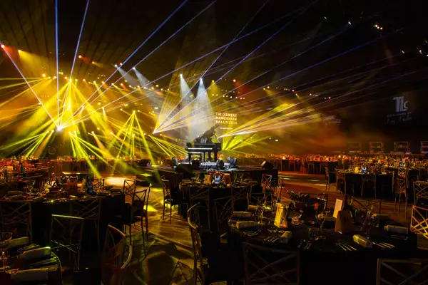 Large circle tables set up in the Warehouse for the Great Mancunian Ball. There are yellow laser lights and a grand piano in the centre.
