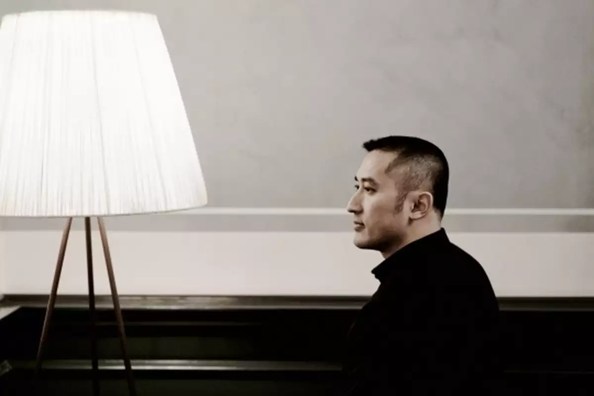 Huang Ruo looking to the side, posing next to a large white lamp