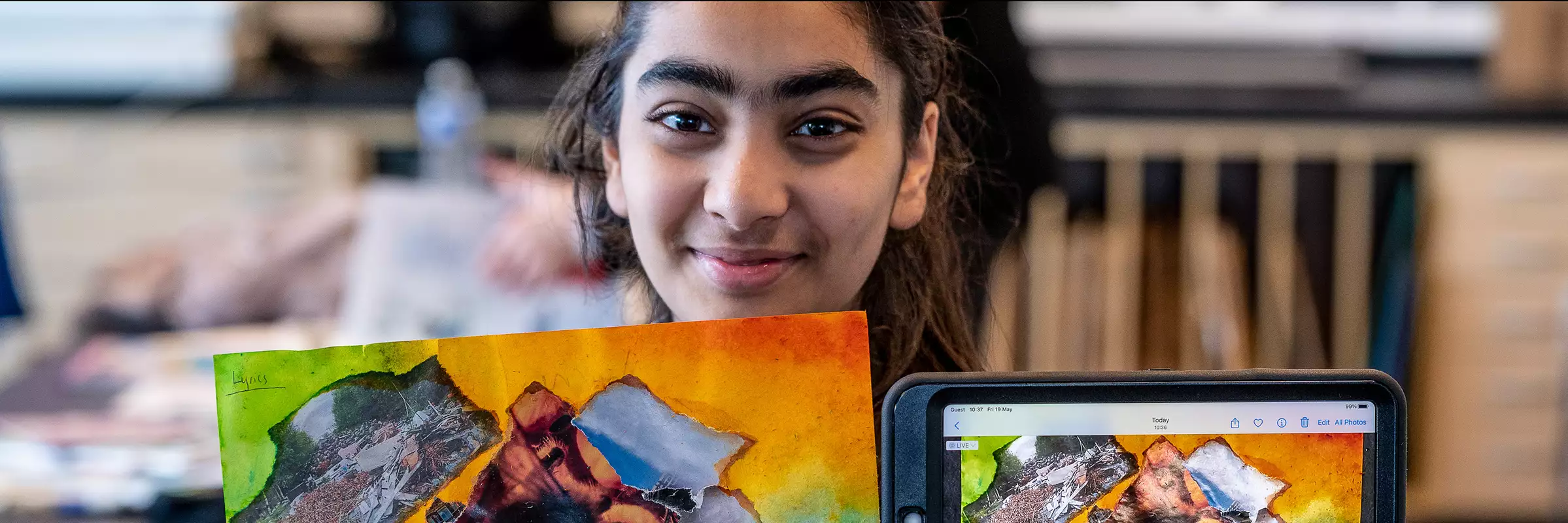 A child holding up their artwork and smiling