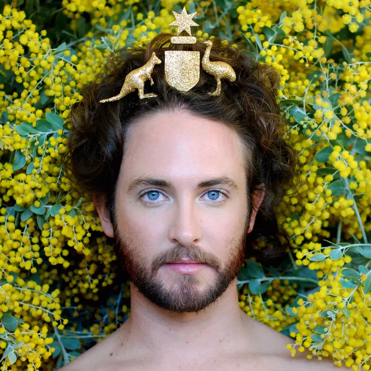 an image of artist Liam Benson with the Australian coat of arms on his head with yellow wattle behind him