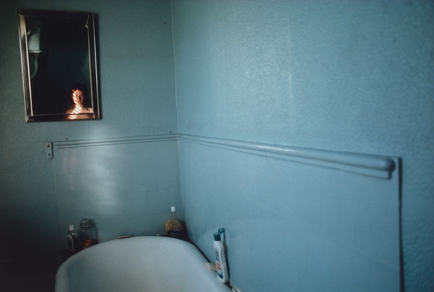 CibaChrome colour photograph of a blue bathroom. See a woman's / the photographer's reflection in a small mirror