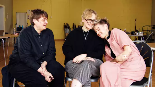 Maxine Peake, Sarah Frankcom and Imogen Knight sat on chairs smiling in a yellow rehearsal room