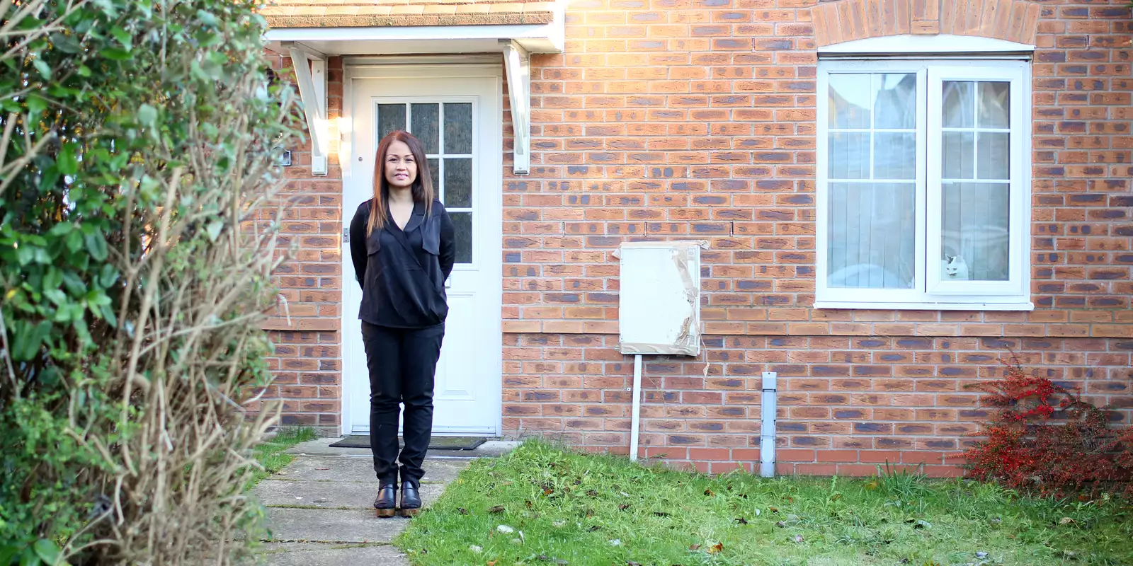 A woman wearing black, standing on a stone path in front of her Cheetham Hill home