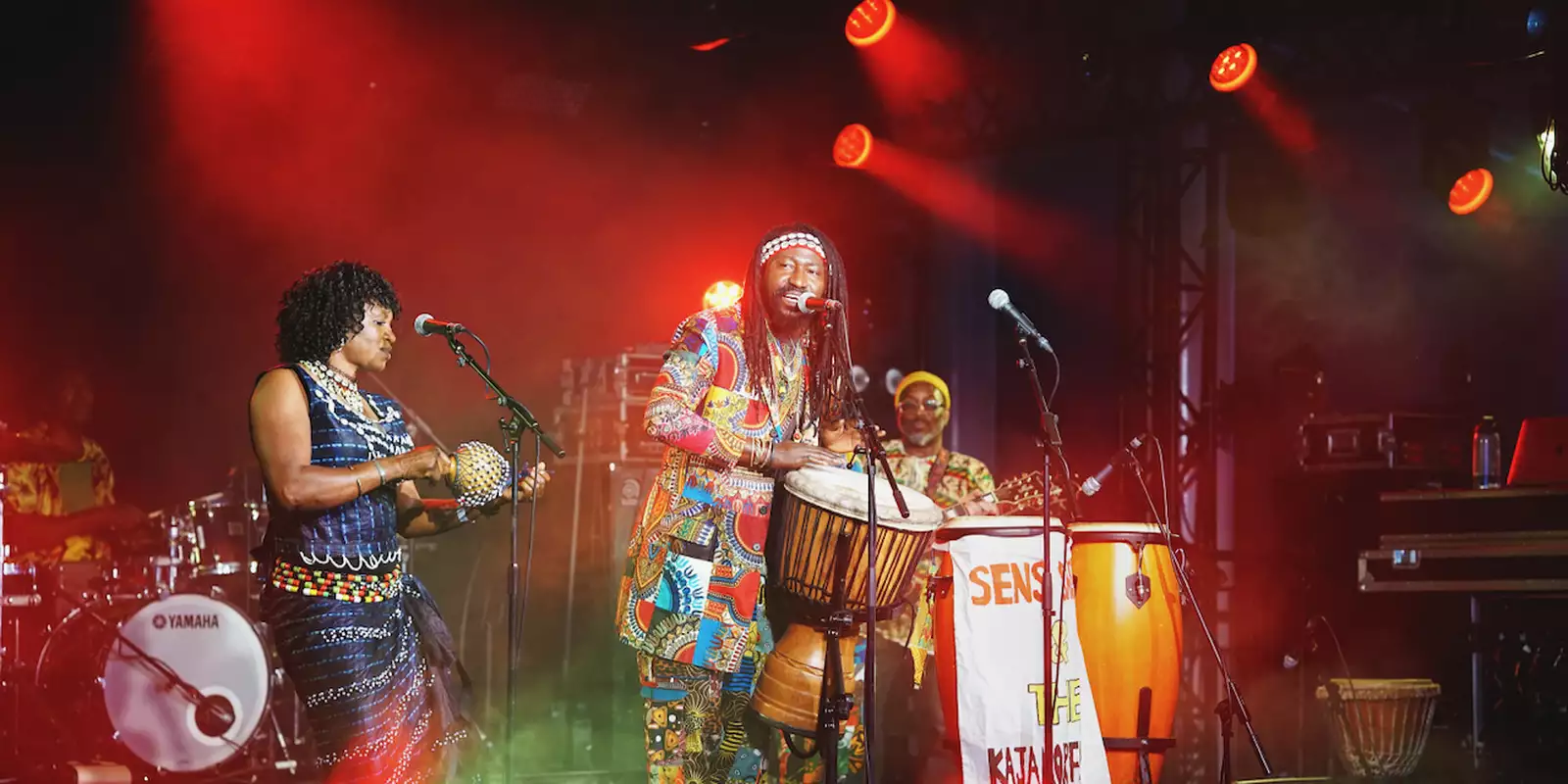 Two members of Sens Sagna & the Kajamor Family performing on the stage at Festival Square. The lighting is red.